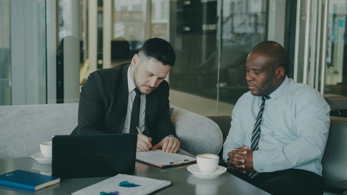 Two businessmen signing a document at a table